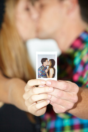 Kissing squared. A young kissing couple holding up a photo booth photograph of them kissing.の写真素材