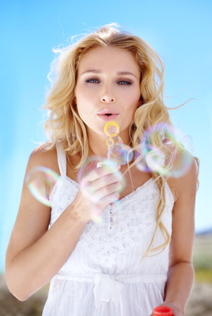 Find your inner child. Pretty young woman blowing bubbles right at you.の写真素材
