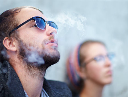 Being cool comes easy to us. a hipster smoking with his girlfriend in the background.の写真素材