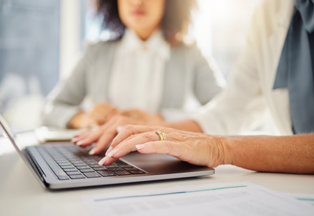 Closeup of caucasian businesswoman typing on a laptop keyboard in an office. Hands of woman pressing buttons to send email and browse the internet while brainstorming alongside a colleagueの写真素材