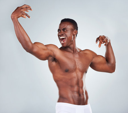 One excited African American fitness model posing topless in a underwear and looking muscular. Happy black male athlete isolated on grey copyspace in a studio wearing boxersの写真素材