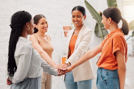 Group of happy businesswomen stacking their hands together in an office at work. Diverse group of...