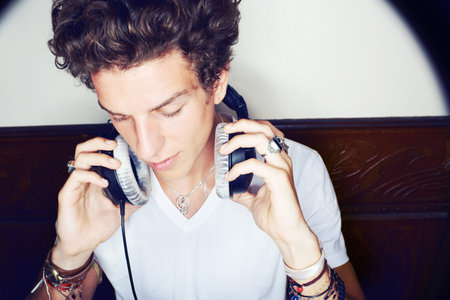 Tune time. A stylish young man putting on a set of headphones while sitting in a hallway.