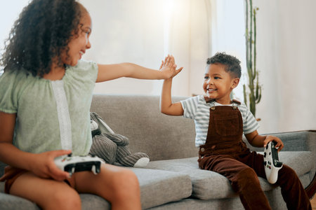 Two happy mixed race siblings sharing a high five on the lounge sofa together while playing fun...