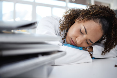 Science, tired and scientist sleeping in lab after working on innovation experiment, test or research. Exhausted, burnout and professional female scientific employee taking nap on desk in laboratory.の写真素材