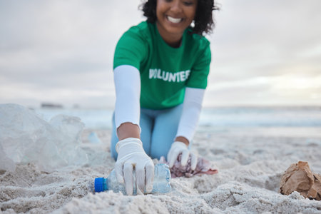 Hand, bottle and a volunteer woman on the beach for community, charity or activism during a clean up. Cleaning, environment and plastic with a female picking up plastic litter or polution on a coastの写真素材