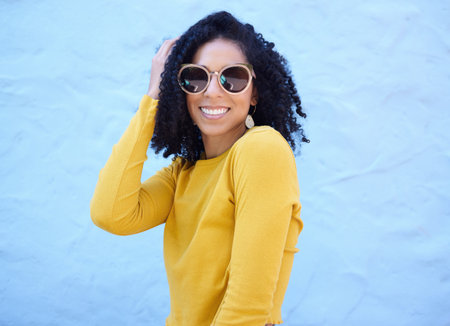 Fashion sunglasses, portrait and black woman on blue background, excited face and trendy cool clothes. Summer, shades and happy girl model smile with vision, yellow color style and urban wall mockupの写真素材