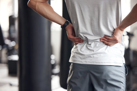 Closeup of one mixed race man holding his sore lower back while exercising in a gym. Guy suffering...