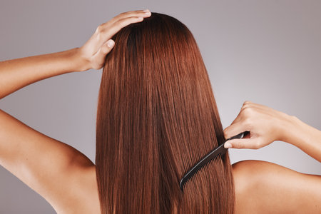 Beauty, comb and woman doing haircare in a studio with a brazilian, keratin or botox treatment. Health, hygiene and back of female model with a long, healthy and shiny hair style by a gray backgroundの写真素材