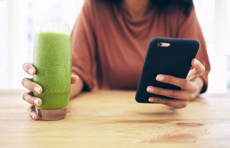 Hands, glass and phone with a black woman in the kitchen of her home for health, weight loss or nutrition. Mobile, smoothie and wellness with a female posting a status update on social mediaの写真素材