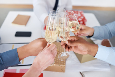 Closeup of group unknown business people sitting together and toasting with champagne glasses for Christmas in office. Team of colleagues celebrating successful year in festive holidays with alcoholの写真素材