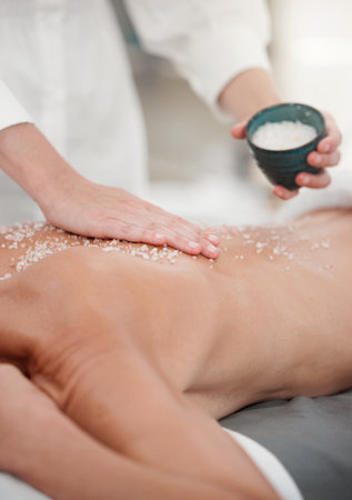 Scrubbing away the dead skin. a woman having a salt scrub rubbed into her back by a masseuse.の写真素材