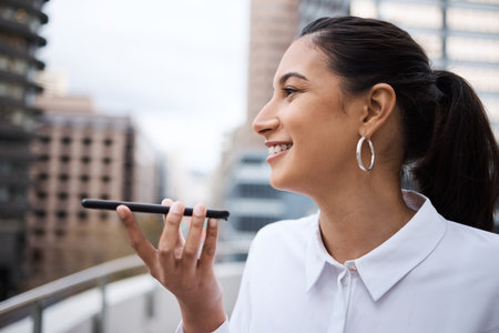 Sending a few voice recordings to her colleagues. a young businesswoman using a cellphone while...