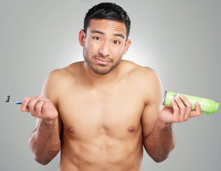 Should I shave it all off. Studio shot of a handsome young man shaving against a grey background.の写真素材