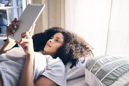 Tablet, black woman and relax in bed in bedroom for social media, texting or internet browsing in...