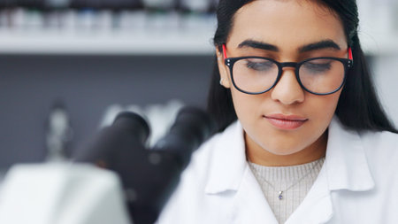 Closeup of a young female scientist using a microscope analysing medical test results or samples in...