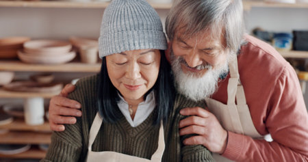 Senior couple, hug and pottery studio work for clay sculpture, product manufacturing and mud design. Asian man, creative woman or retirement elderly in small business, workshop or Japanese art studioの写真素材