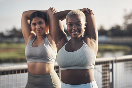 Stretch, your body will thank you later. two young women stretching while outside for a workout.の写真素材