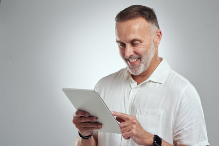 All I do is tap here and there and voila. Studio shot of a mature man using a digital tablet against...