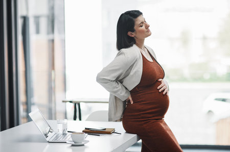 Being pregnant is no piece of cake. a pregnant young businesswoman feeling unwell while working in a modern office.の写真素材