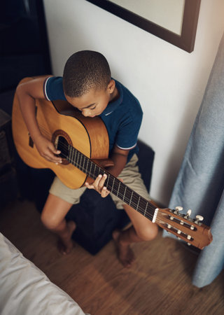 I want to be a guitarist just like my dad. a young boy playing the guitar at home.
