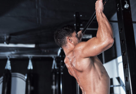 Nothing lifts you up like good health. a young man lifting doing pull ups at a gym.