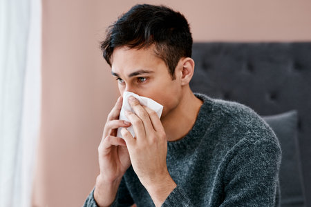 Where could I have caught this flu from. a young man blowing his nose while recovering from an illness in bed at home.の素材 [FY310199123670]