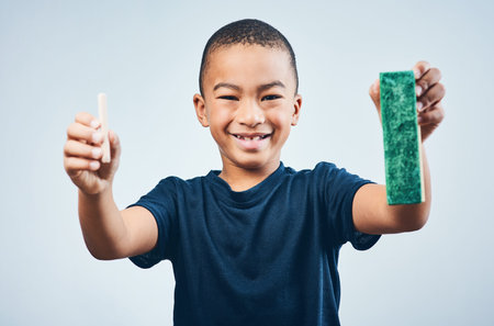 Lets get ready to learn. Studio shot of a cute little boy chalk and a duster against a grey background.の写真素材