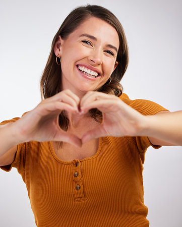 Its love that makes the world go round. Studio shot of a young woman showing a heart sign with her hands against a white background.の写真素材