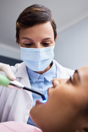 Finely skilled in the art of creating smiles. a dentist using a curing light on a patient during orthodontic treatment.の写真素材