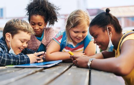 Come on, beat them. a diverse group of children huddled together and using game boys to play games at school.の写真素材