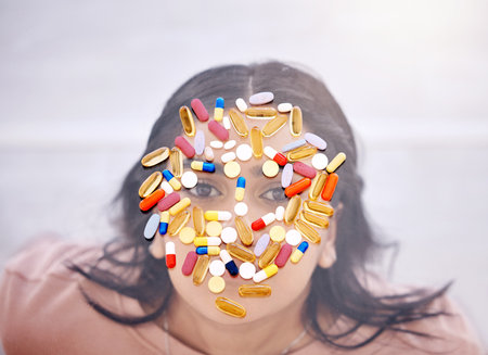 Addiction, pills and medicine on woman face as drug abuse from overhead view looking serious and covered by medication. Tablets, issue and antibiotics problem by mental health patient or femaleの写真素材