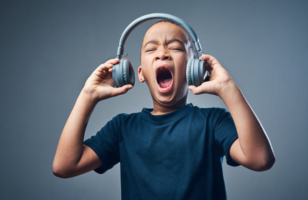 With big bass comes big fun. Studio shot of a cute little boy using headphones with his mouth open against a grey background.の写真素材