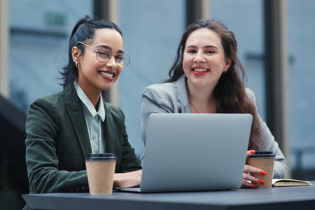 The task is lighter when the load is shared. two young businesswomen using a laptop during a meeting at a coffee shop.の写真素材