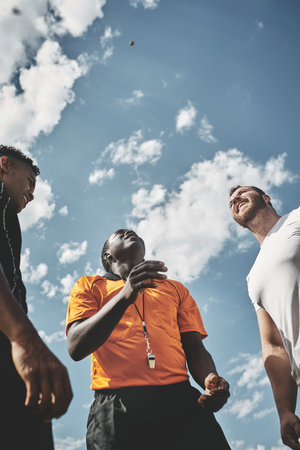 Call it. Low angle shot a referee flipping a coin among two rugby team captains to see who will start the kickoff of the match outside during the day.の写真素材