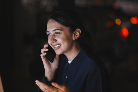 Office, talking and business woman on a phone call for virtual meeting, discussion and planning at night. Communication, social networking and girl chat, speaking and in conversation on smartphoneの写真素材