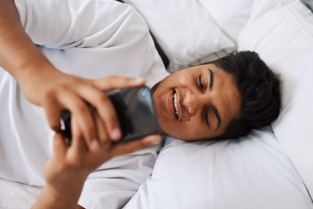 Shes the only one who keeps me up this late. a young man using his cellphone while lying on his bed.の写真素材