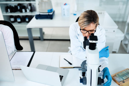 The scope of her research is quite vast. a mature scientist using a microscope in a lab.