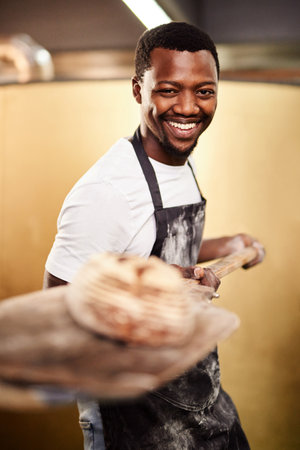 This is my bread and butter. a male baker removing freshly baked bread from the oven.の写真素材