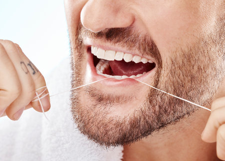 Dental, hygiene and man flossing his teeth in a studio for oral care, grooming or health. Wellness, healthy and closeup of male model doing fresh, clean and natural mouth routine by white background.の写真素材
