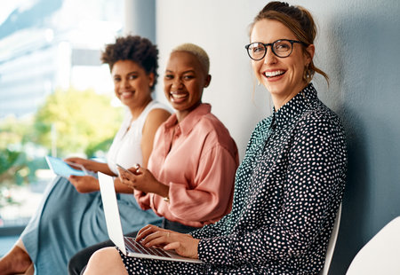 Can you believe theres free wifi here. Cropped portrait of a group of attractive young businesswomen using wireless technology while sitting in line in a modern office.の写真素材