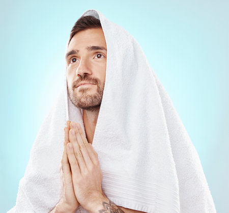 Prayer, thinking and worship with man and towel for hope, spiritual and Catholic faith. Respect, religion and Holy spirit with guy and hands for believer, humble and Christianity with blue backgroundの写真素材