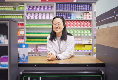 Pharmacy, smile and portrait of asian woman at counter in drugstore, customer service and medical advice in Japan. Prescription drugs, happy pharmacist and inventory of pills and medicine at checkoutの写真素材