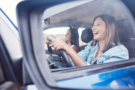 Travel, mirror and friends with women in car driving for road trip, vacation and transportation. Summer break, happy and smile with reflection of girl driver on holiday for journey, auto or directionの写真素材