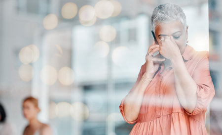 Stress, headache and phone call of senior woman feeling pain, tired or exhausted. Bokeh window, mental health or ceo with depression, anxiety or migraine while talking on mobile with bad news mockup.の写真素材