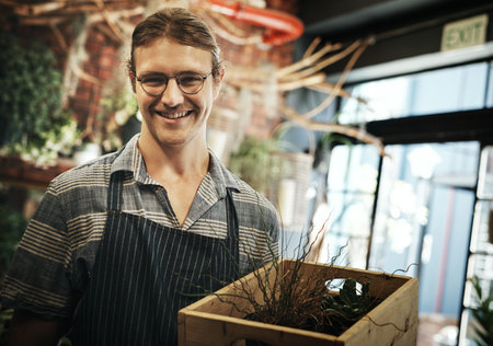 Im happily living on the green side of life. Portrait of a handsome young florist holding a crate full of plants inside of his plant nursery.の写真素材