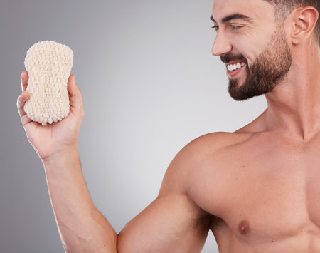 Hygiene, man and sponge for cleaning, smile and wellness with guy on grey studio background. Male, gentleman and skincare for washing, happiness and grooming routine for health, smooth and soft skinの写真素材