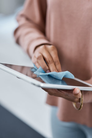 Keep that screen clean. an unrecognisable woman disinfecting her digital tablet while working from home.の写真素材