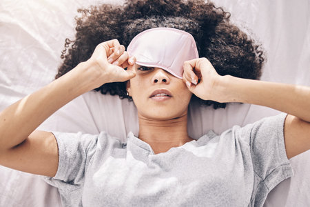 Sleep, relax and black woman with eye mask waking up, dream and refresh body and mind in apartment or hotel. Dreaming, rest and relaxation, tired girl sleeping late on weekend morning in cozy bedroomの写真素材