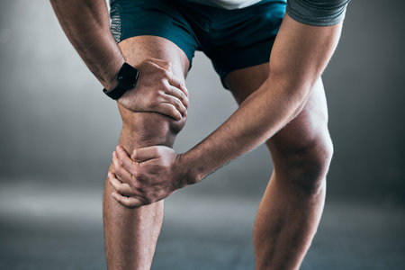 Theres always the risk of injury. an unrecognizable young male athlete holding his knee in pain against a grey background.の写真素材